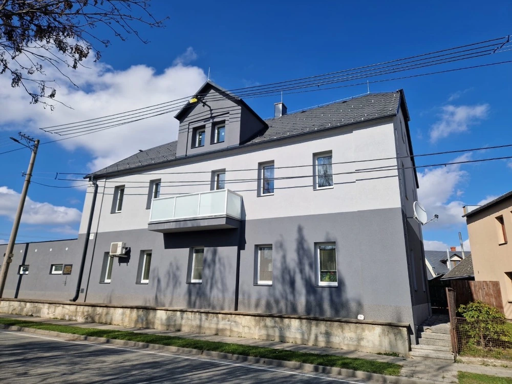 Bytový dům v Hlavnici po renovaci, s novou šedobílou zateplenou fasádou a vyměněnými okny.