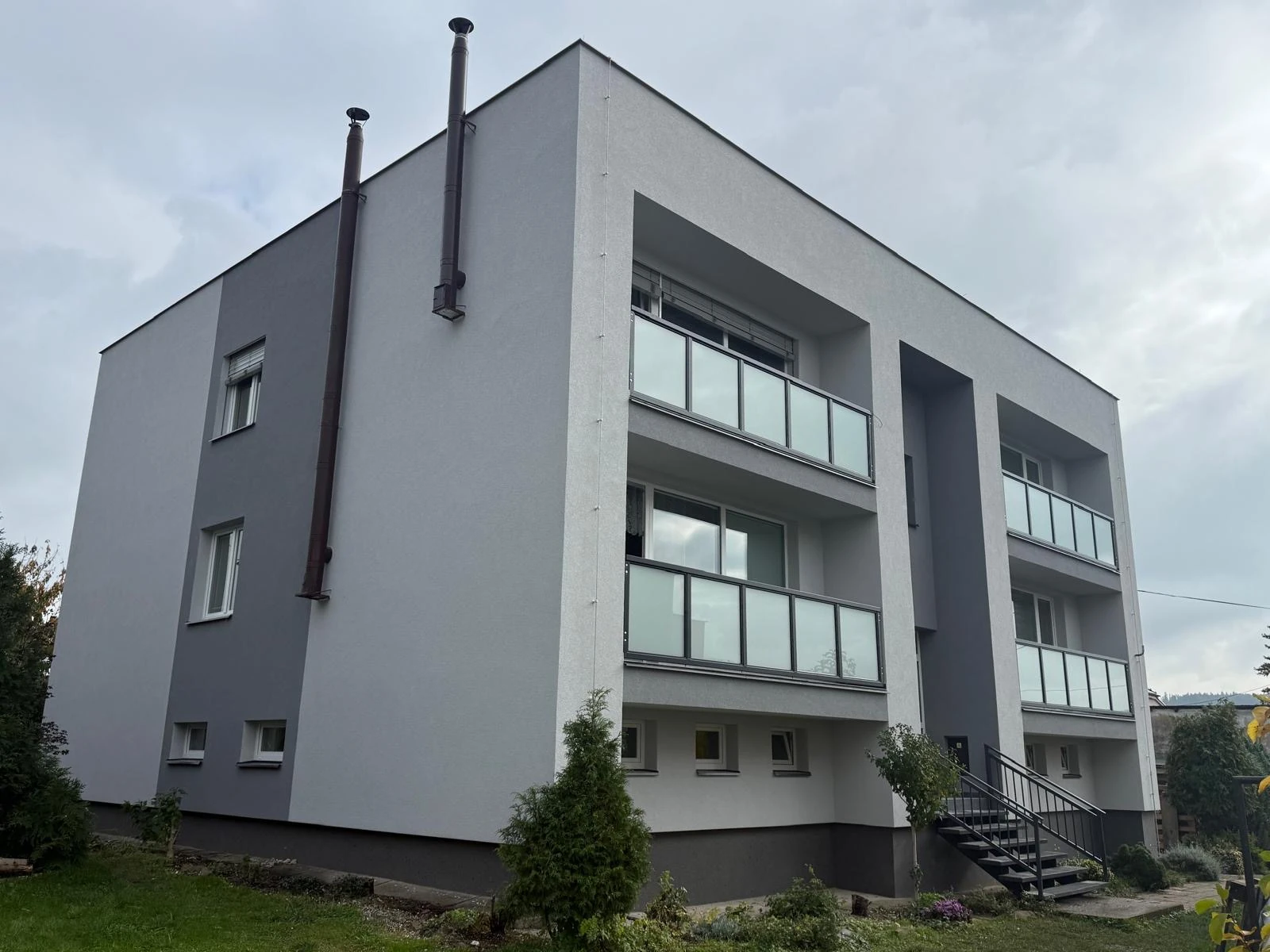 Bytový dům v Uhlířově po komplexní renovaci, s novou šedobílou fasádou, upravenými balkony a venkovními žaluziemi.